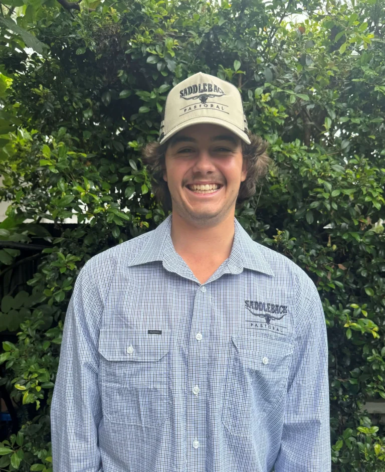 A person wearing a "Saddleback" cap and shirt stands smiling in front of a leafy background.